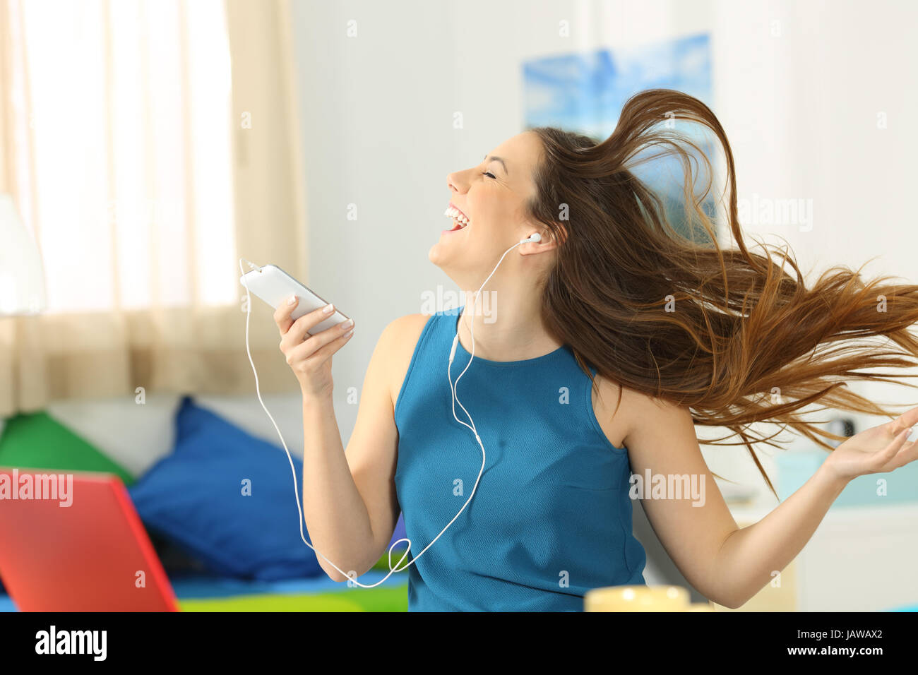 Teen ascoltare musica e ballare tenendo un telefono intelligente con i suoi capelli in movimento nella sua camera da letto Foto Stock