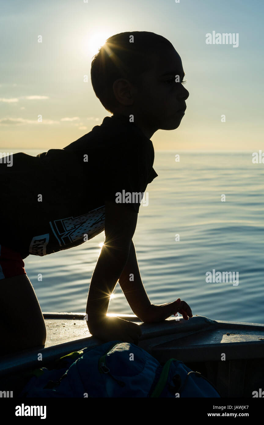 La silhouette di un ragazzo aborigeno della scansione del orizzonte dell'oceano al tramonto. Foto Stock
