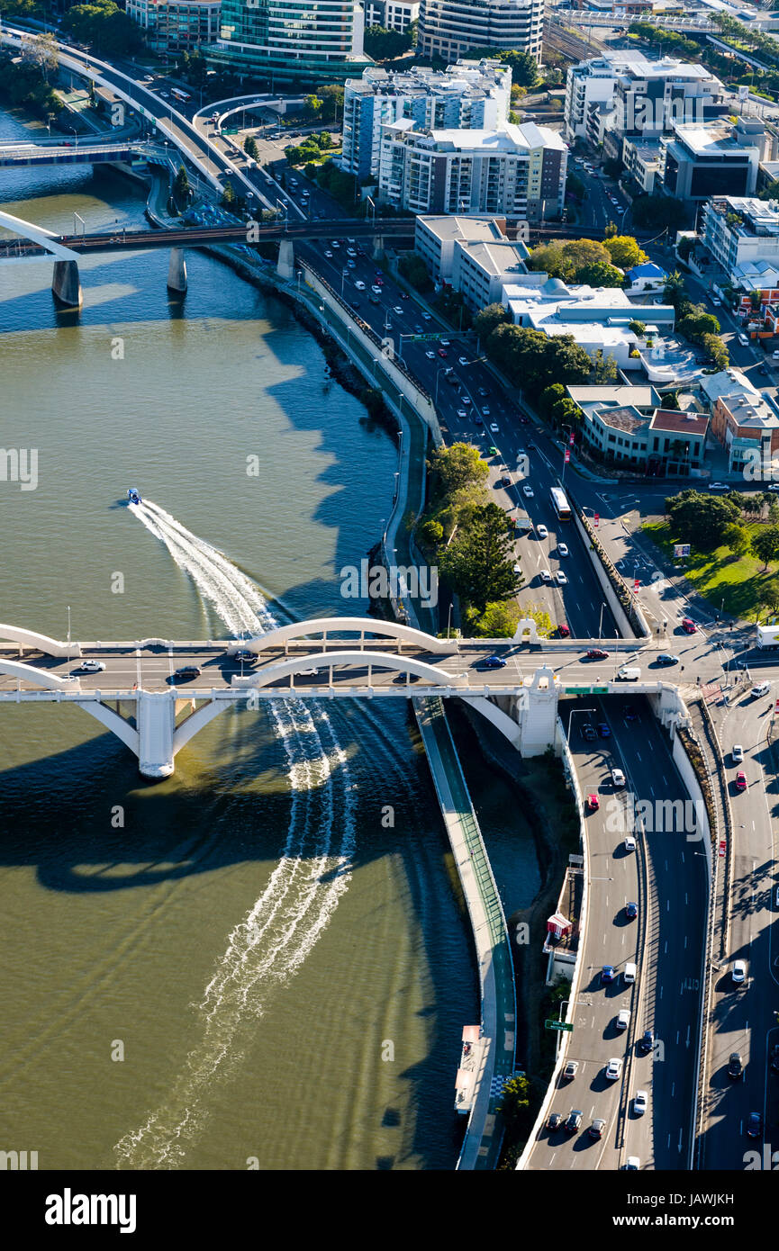 Un motoscafo passa al disotto di un ponte sul fiume lasciando il traffico su una superstrada dietro. Foto Stock