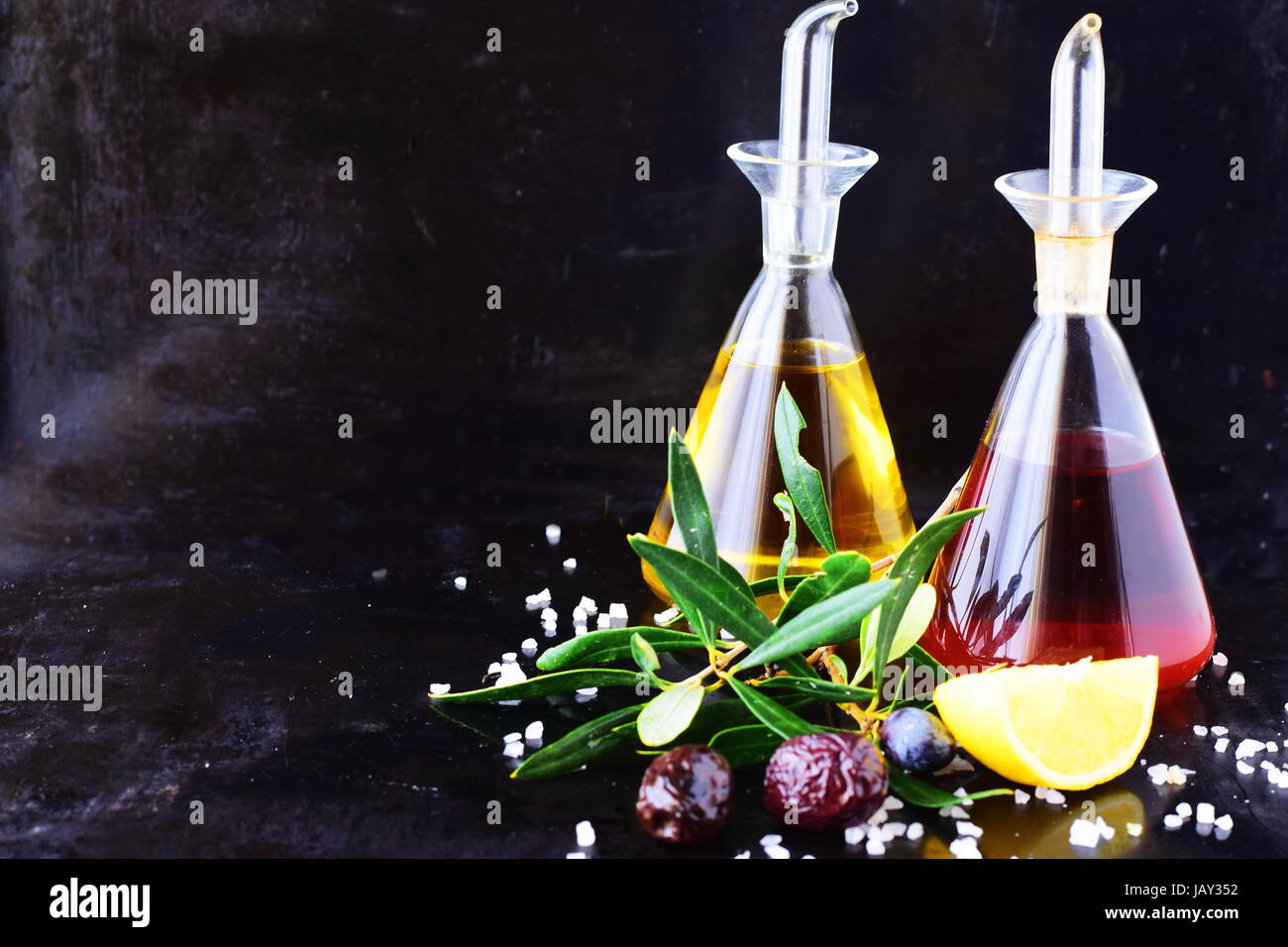 Grigio sfondo astratto con olio di oliva e aceto di vino vasi di vetro con limone, sale marino, aglio e olive branch. Spazio per il testo. Foto Stock