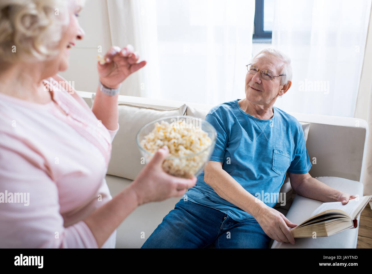 Senior donna mangiare popcorn, uomo libro lettura dietro Foto Stock