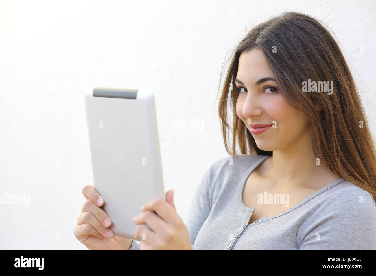 Pretty Woman tenendo un tablet e guardando la telecamera su un muro bianco Foto Stock