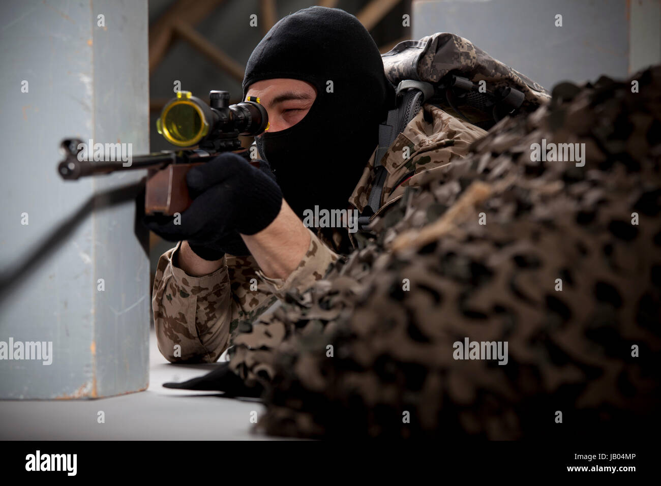 Uomo armato in passamontagna nascosto dietro un muro Foto stock