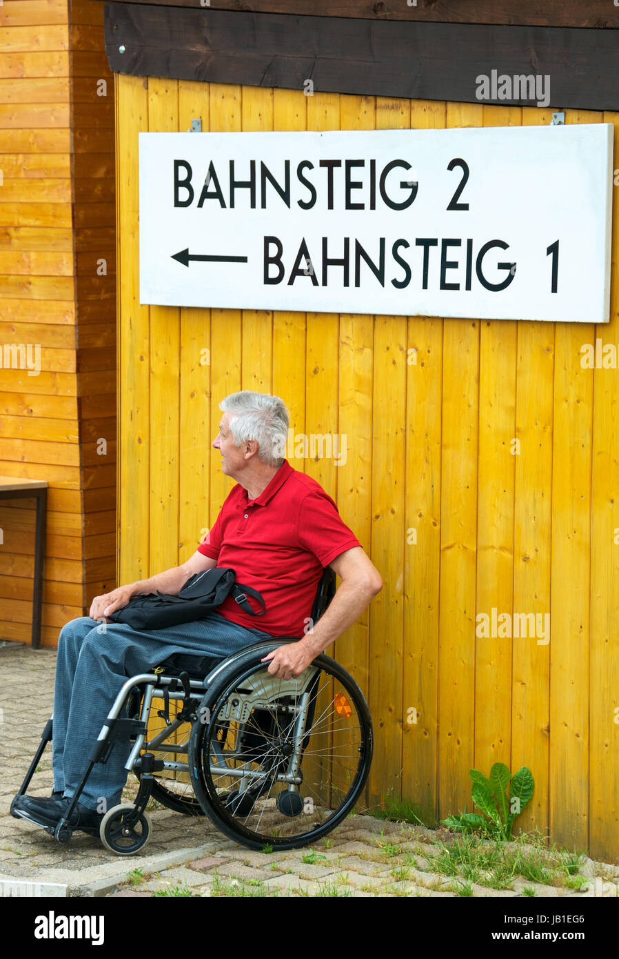 Rentner im Rollstuhl wartet un einem Bahnsteig Foto Stock
