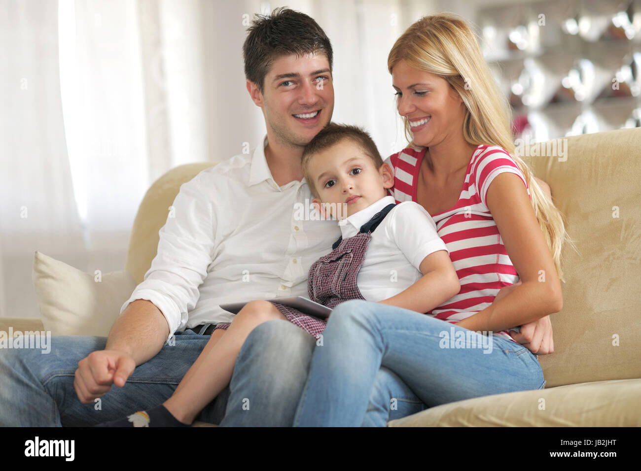 Felice famiglia giovane utilizzando computer tablet a casa moderna per la riproduzione di giochi e istruzione Foto Stock