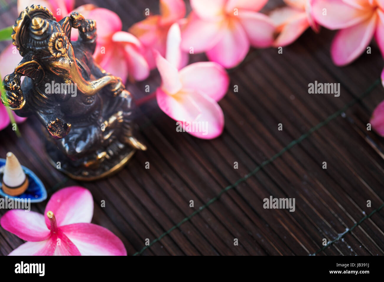 Statua di Ganesha Induismo Indiano Dio della sapienza e della prosperità e heap di plumeria frangipani fiori Foto Stock