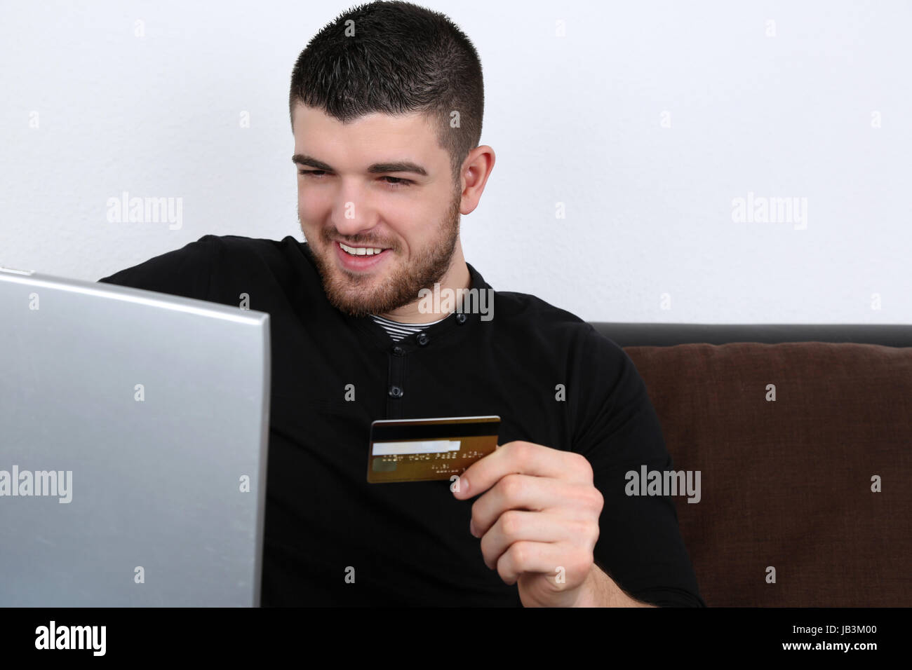 Ein junger Mann mit Laptop kauft im Internet mit einer Kreditkarte ein Foto Stock