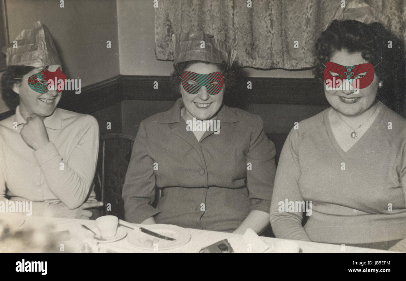 Fotografia di tre donna alla tabella pub, 1950, con cracker di Natale e la festa di carta cappelli, e indossano maschere per occhi, godendo di se stessi. Una versione come originale e un altro con maschere colorate a mano. Foto Stock