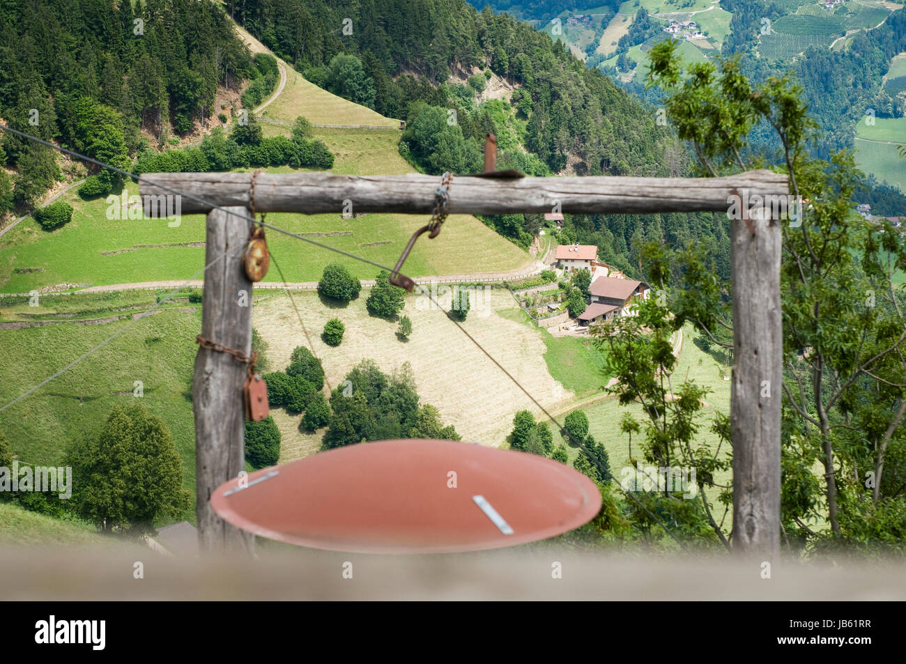 Landschaftsaufnahme in Südtirol oberhalb der a monte Bergstation muta: Blick durch ein hölzernes Holzgestell einer bergbäuerlichen Lasten-Seilbahn auf einen Steilhang mit hinaufführender Straße Foto Stock