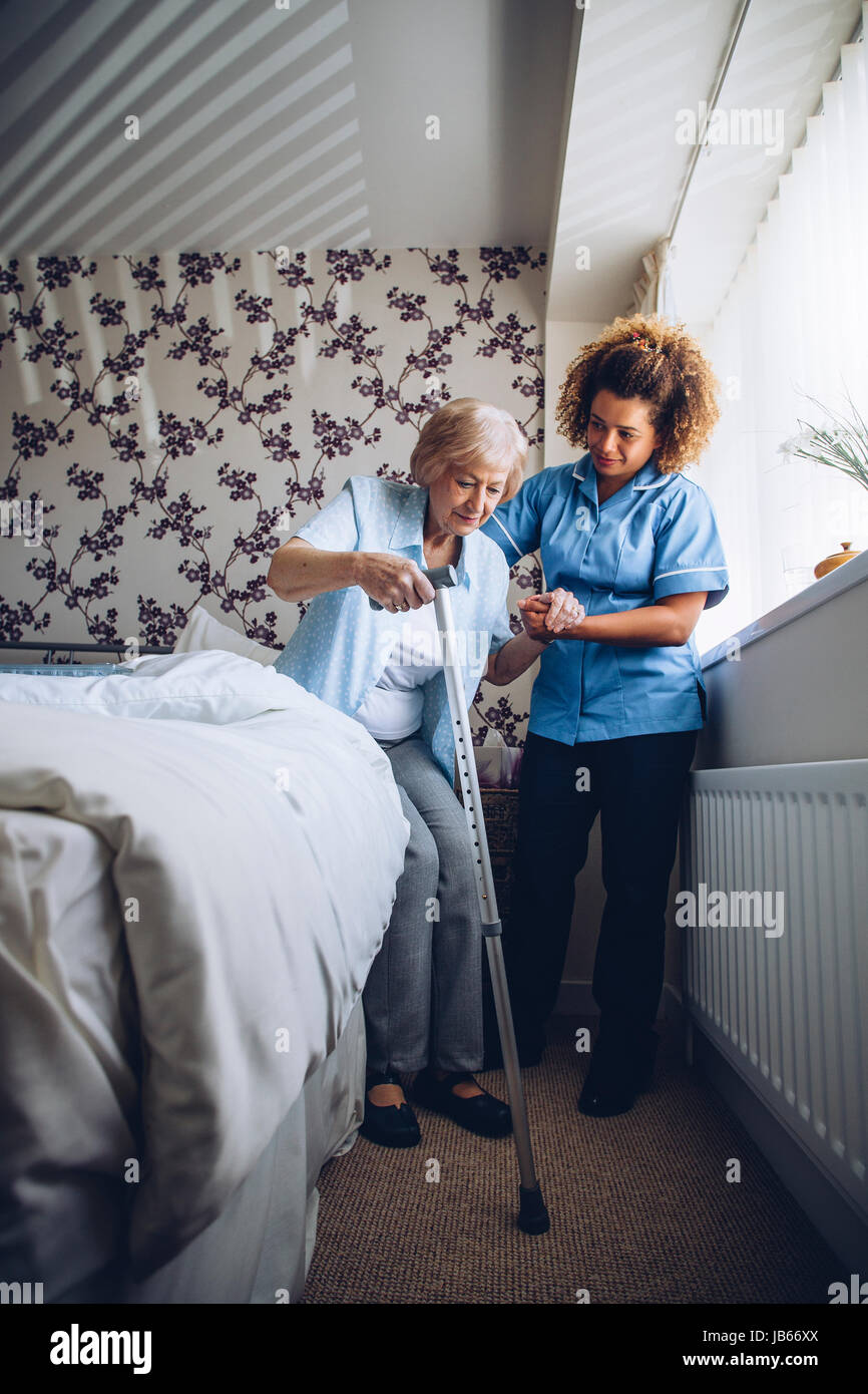 Home Caregiver aiutando un senior donna alzarsi dal suo letto con un bastone da passeggio. Foto Stock