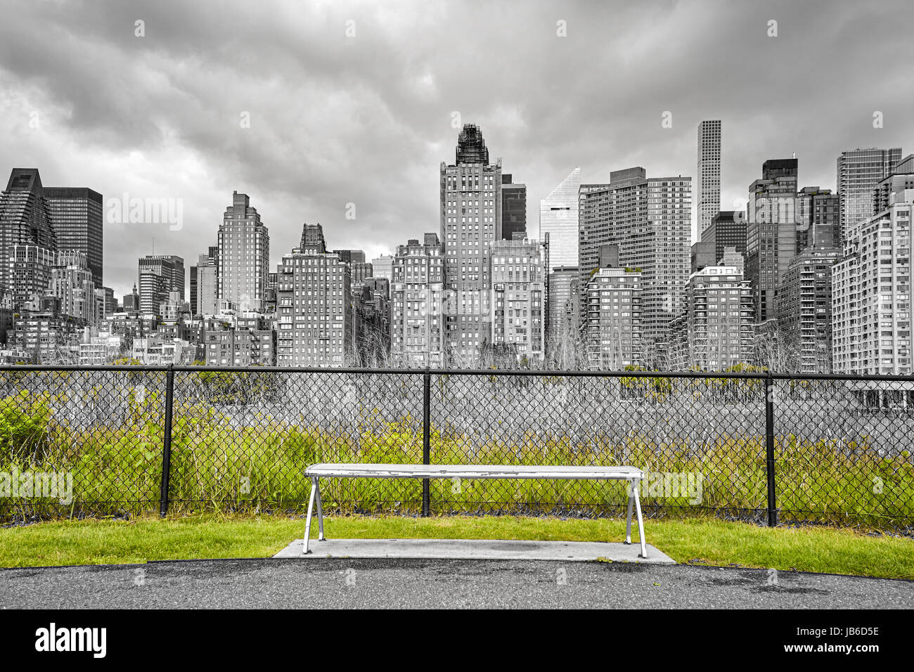 Panca in Roosvelt Island promenade, focus su edifici, foto in bianco e nero con solo erba verde a colori, New York City, Stati Uniti d'America. Foto Stock