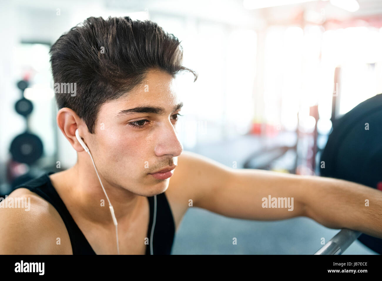 Uomo ispanico in palestra in appoggio, gli auricolari nelle orecchie,l'ascolto mus Foto Stock