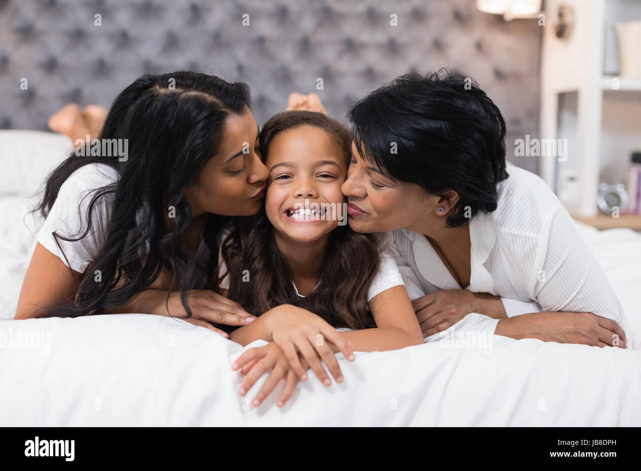 La nonna e la madre baciare sorridente ragazza mentre giaceva sul letto di casa Foto Stock