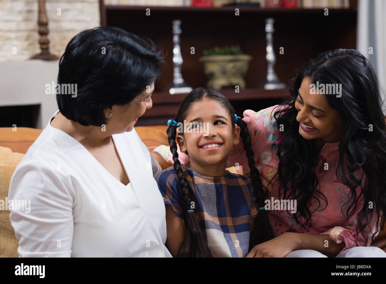 Carina ragazza sorridente con la madre e nonna seduti insieme sul divano di casa Foto Stock