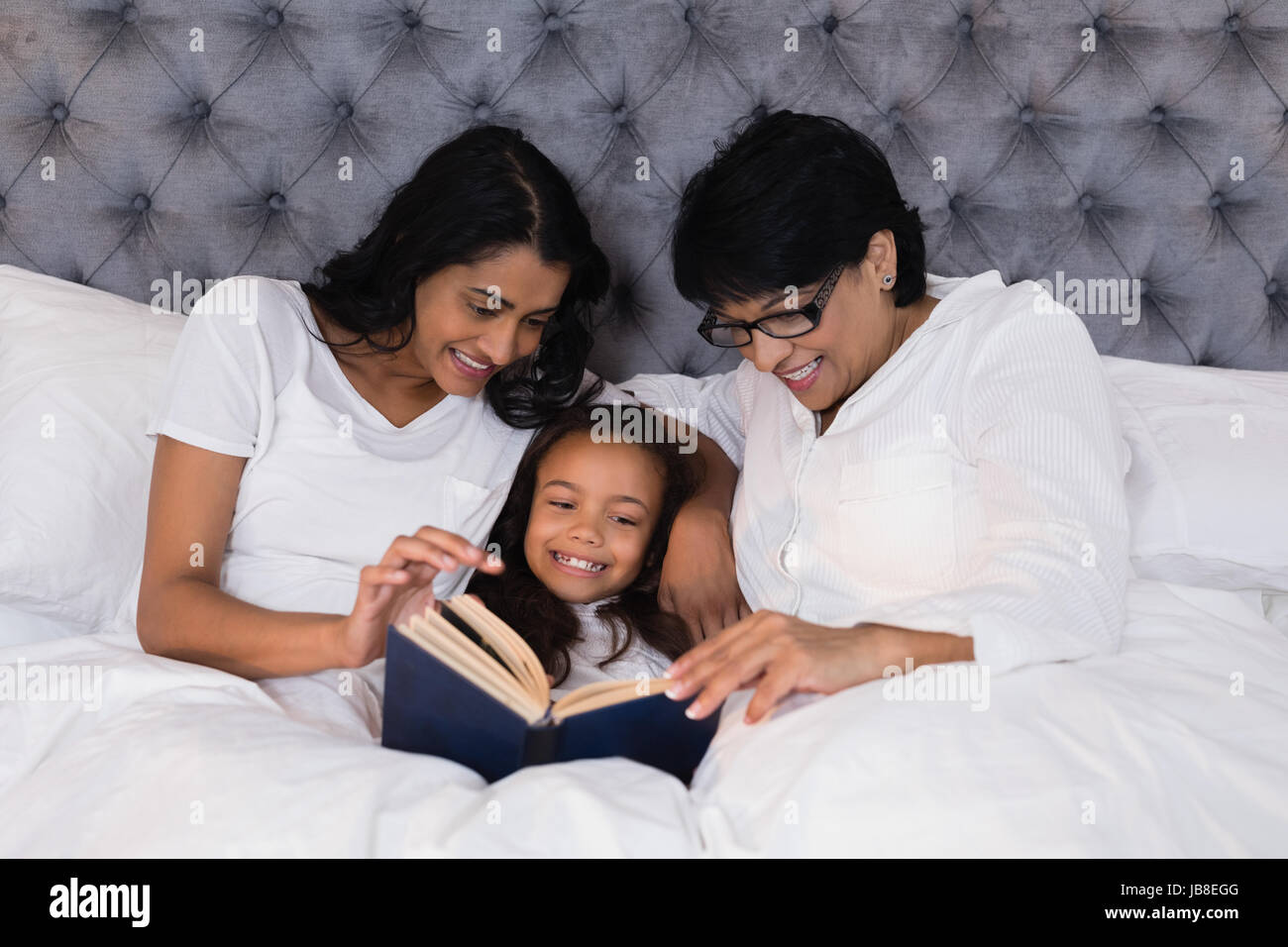 Sorridente multi-generazione famiglia libro lettura mentre è appoggiato sul letto di casa Foto Stock