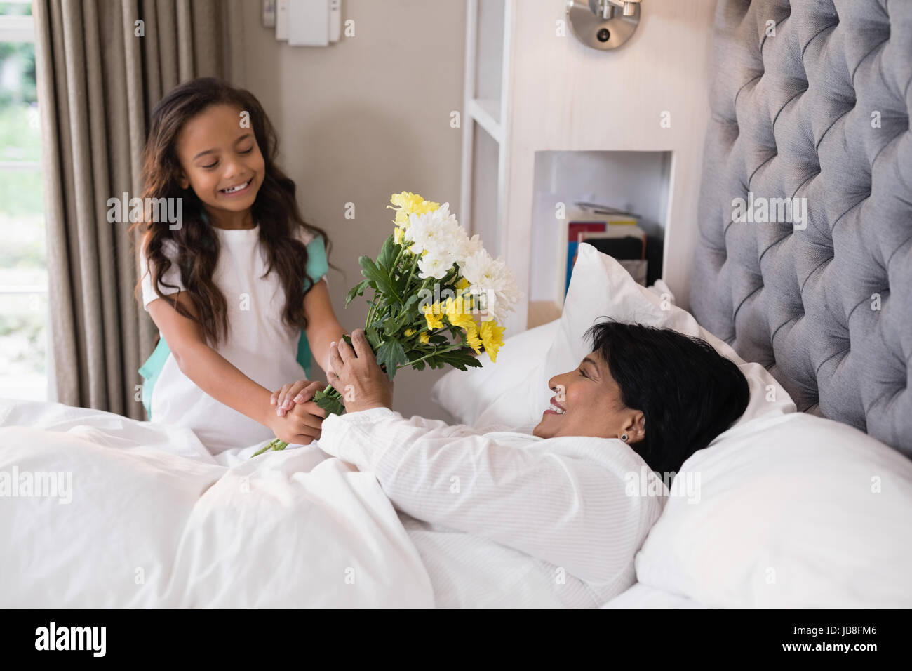 Angolo di Alta Vista della ragazza sorridente dando bouquet per malati nonna a casa Foto Stock