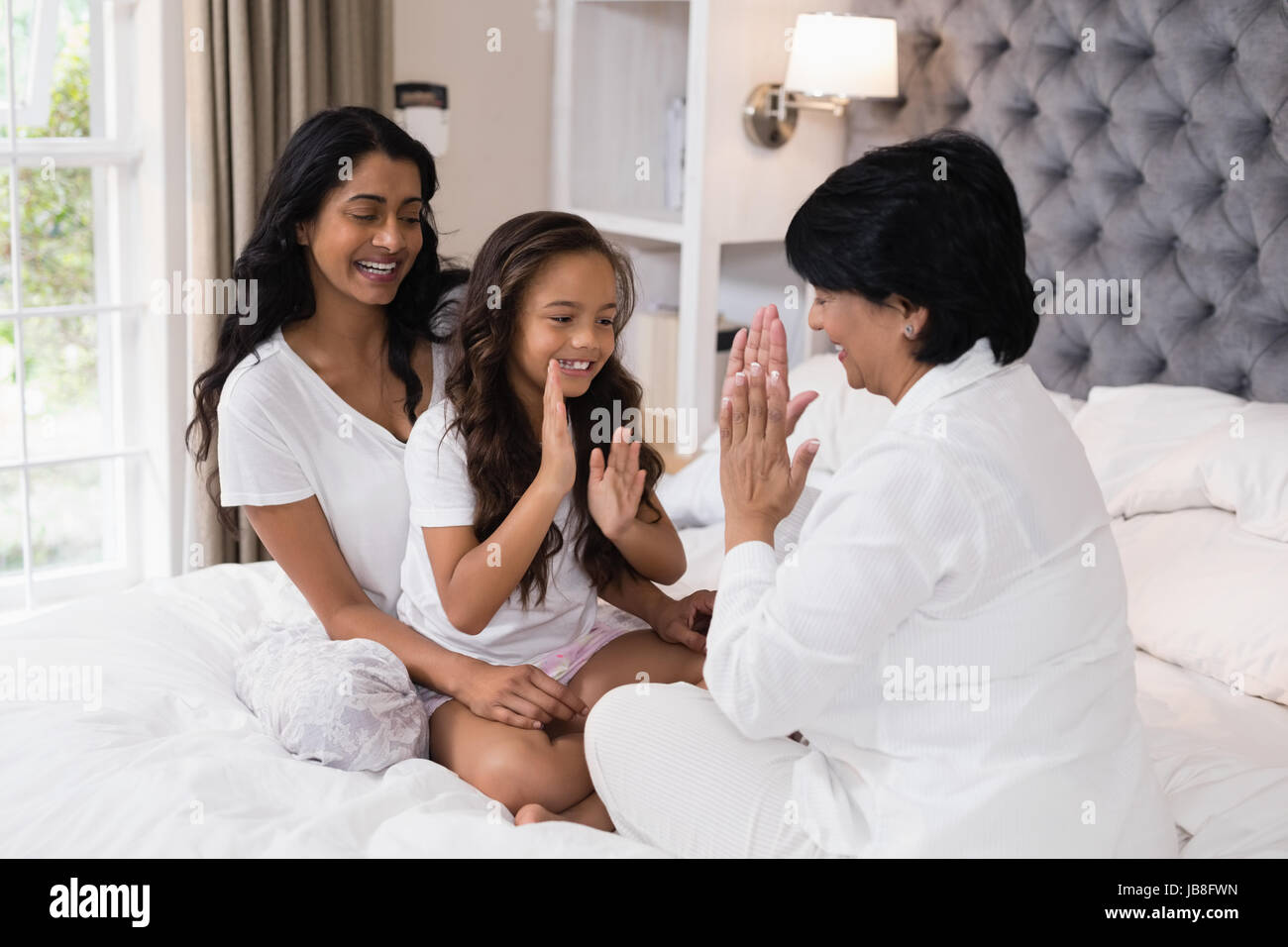 Felice multi-generazione famiglia giocando patty la torta su letto di casa Foto Stock
