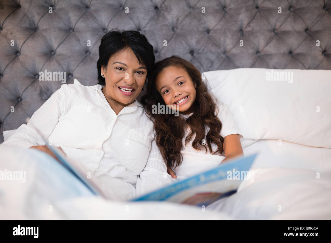 Ritratto di felice la nonna e la nipote la lettura di un libro sul letto di casa Foto Stock
