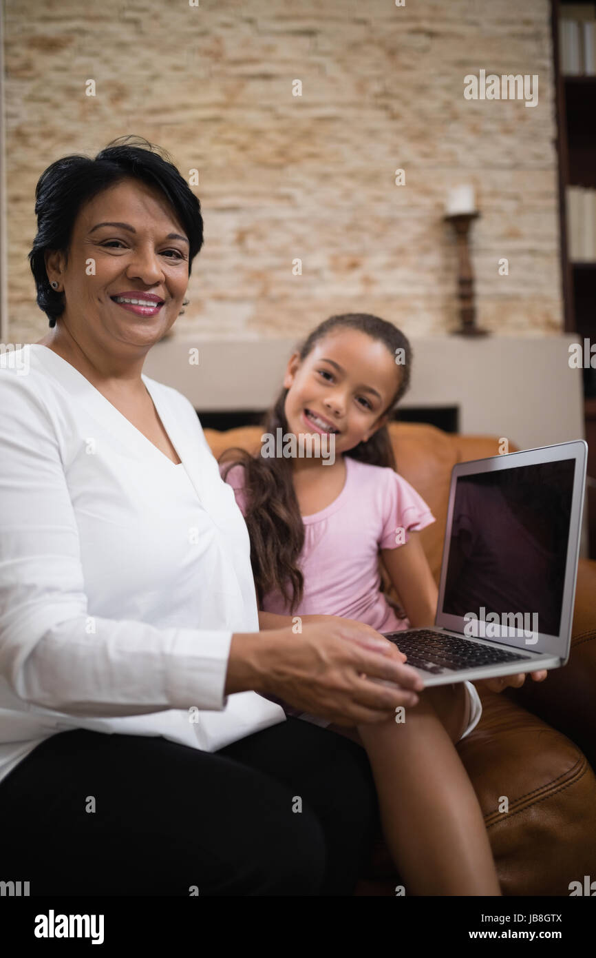Ritratto di donna sorridente con il nipote holding laptop stando seduti sul divano di casa Foto Stock