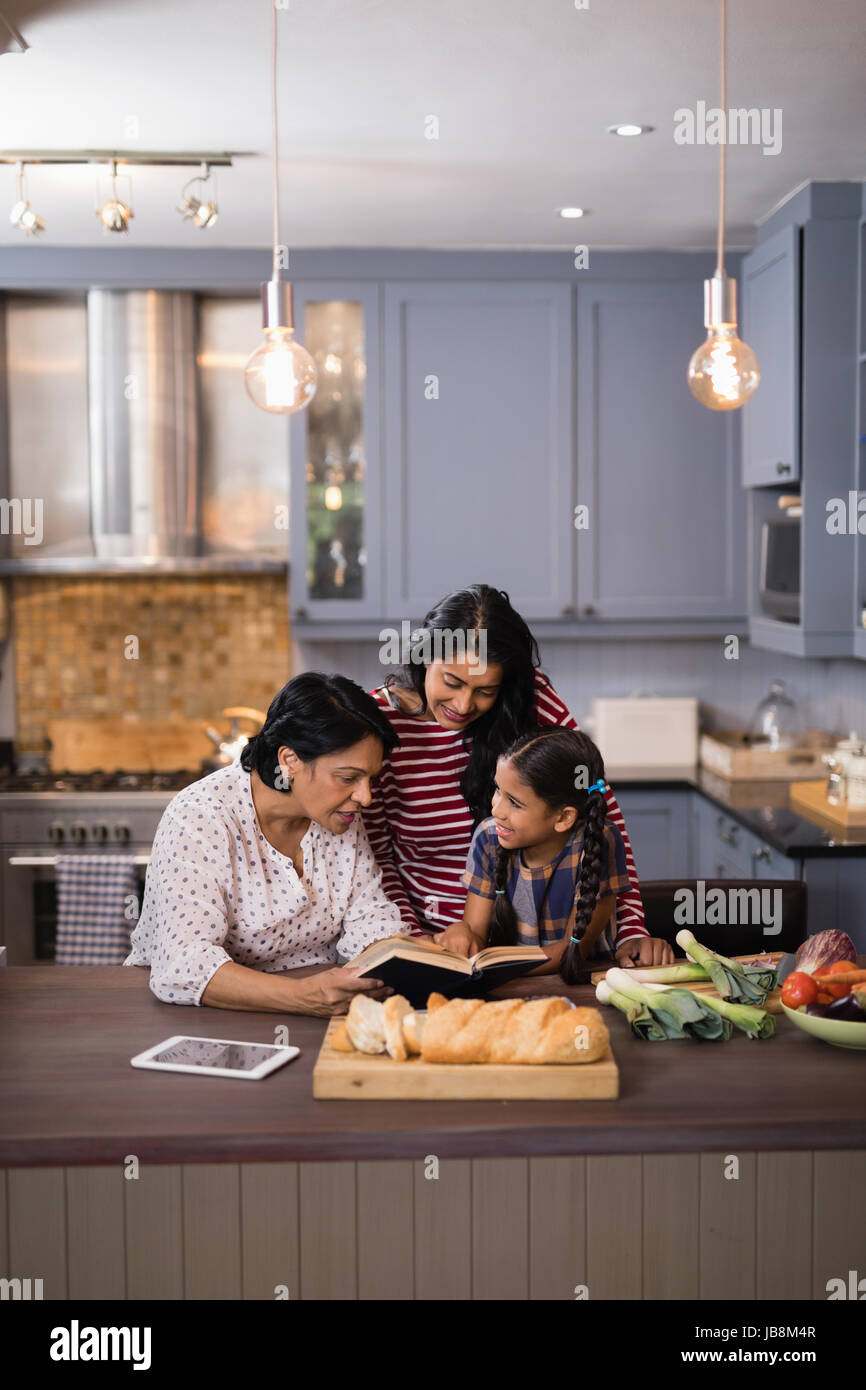 Multi-generazione famiglia libro lettura insieme nella cucina di casa Foto Stock