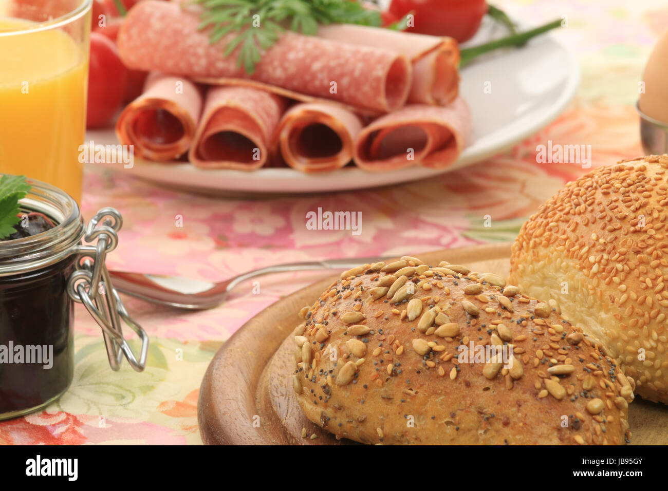 Ausschnitt eines Frühstückstisches mit Brötchen, Aufschnitt, marmellata, Tomaten und Orangensaft Foto Stock