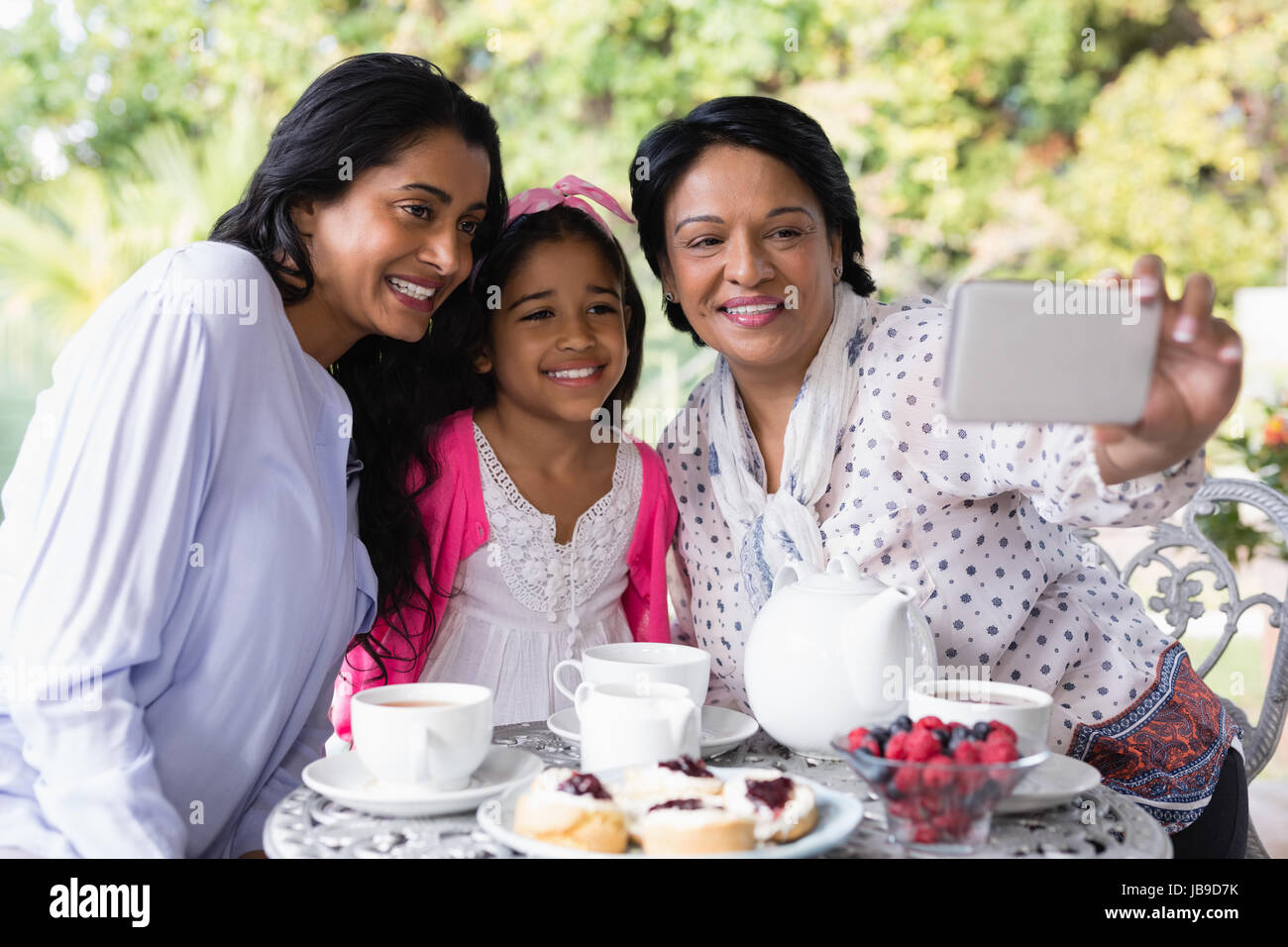 Sorridente multi-generazione famiglia tenendo selfie seduti insieme da tavolo per la colazione a casa Foto Stock