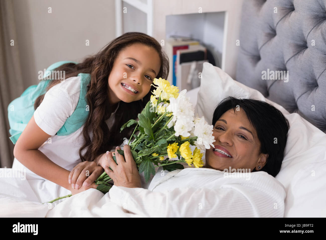 Angolo alto ritratto della nonna sorridente e nipote con bouquet di fiori sul letto di casa Foto Stock
