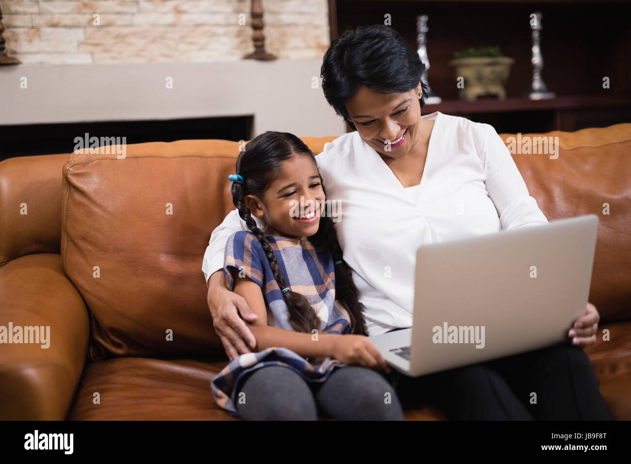 Donna sorridente con il nipote utilizzando laptop stando seduti sul divano di casa Foto Stock