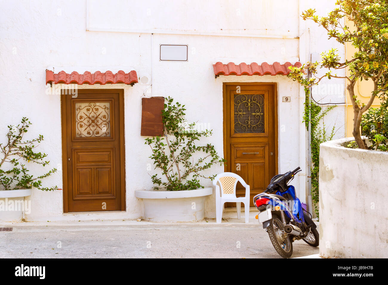 Rethymno, Grecia - 3 Maggio 2016: blu sport motocross moto parcheggiata di fronte bianco muro di pietra con porte di legno intagliato. Resort classic architetto greco Foto Stock