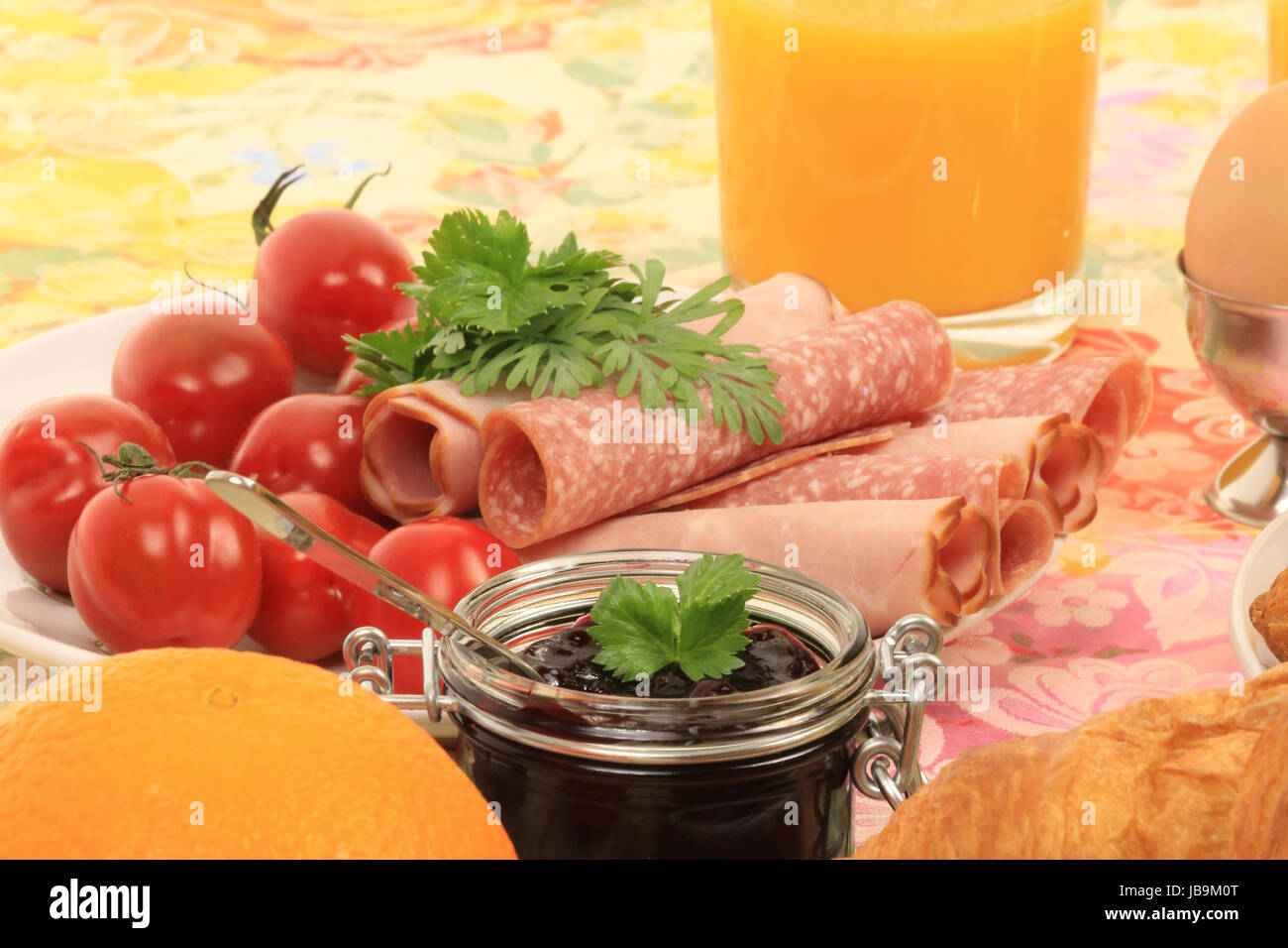 Ausschnitt eines Frühstückstisches mit Croissant, Aufschnitt, marmellata, Tomaten, arancio, Ei und Orangensaft Foto Stock