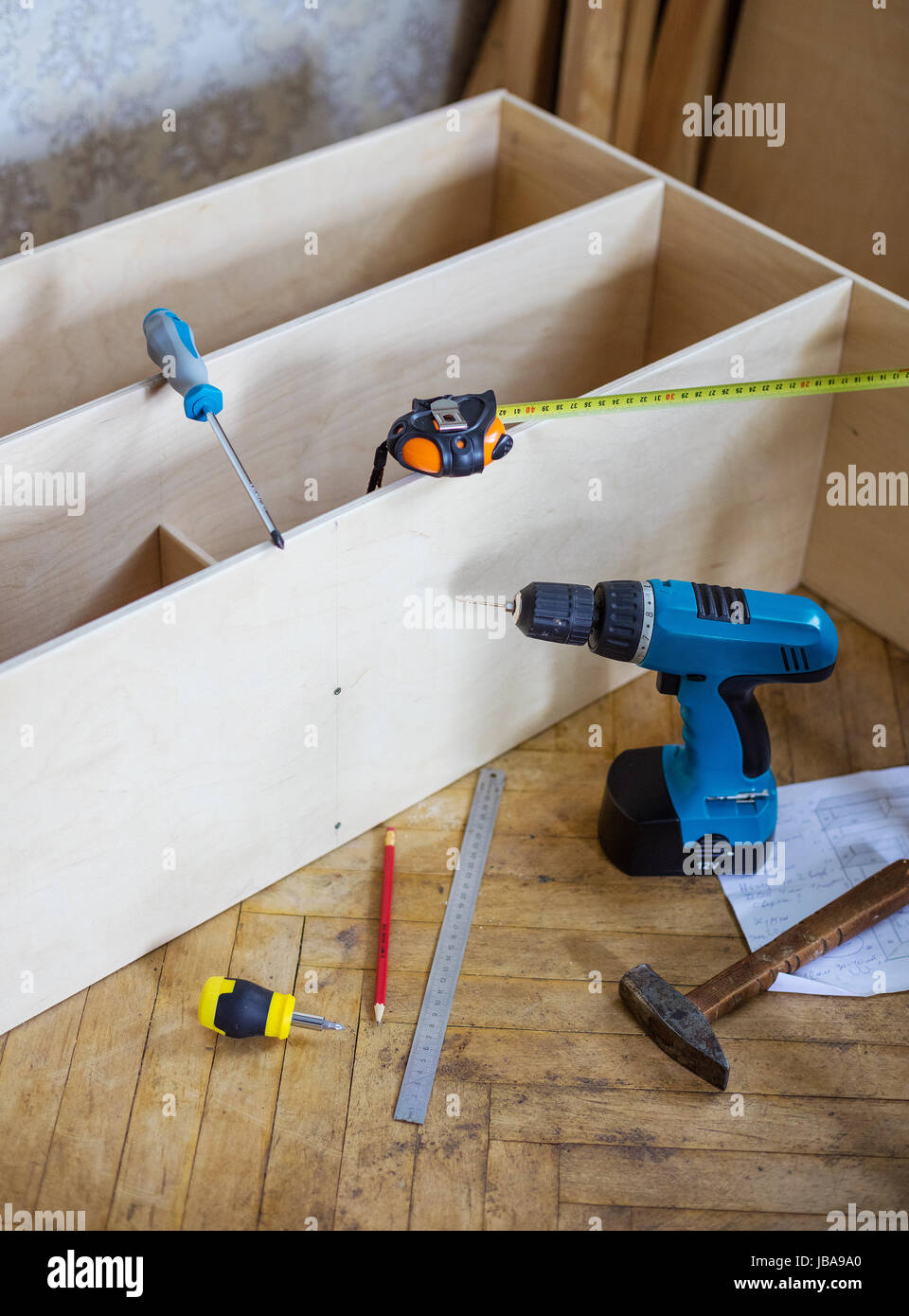 Incompiuta scaffalatura e strumenti sul pavimento in ambiente domestico. Cacciavite elettrico, martello, righello matita, progetto, nastro di misurazione, avvitatori manuali bes Foto Stock