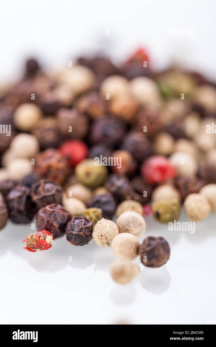 Sullo sfondo di un intero fresco essiccato pepe nero in grani sparsi su una superficie bianca per uso come una piccante di spezie ed aromi in cucina Foto Stock