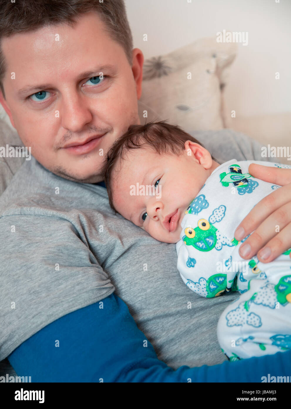 Ritratto di 1 mese vecchio baby boy nel suo papà di braccia, quasi addormentato in casa. Foto Stock