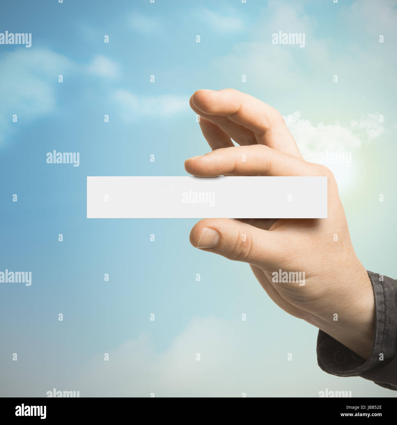 Una mano che tiene una scheda vuota con un cielo blu sullo sfondo con nuvole e sole. Concetto di comunicazione per affari o Marketing Foto Stock
