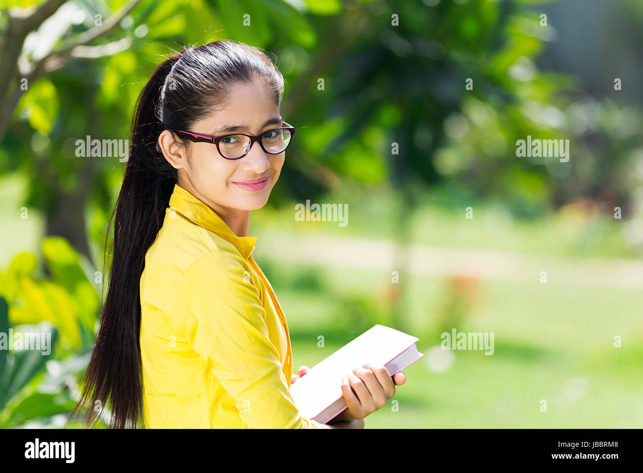 1 teeanger indiano ragazza studente di college azienda prenota istruzione in piedi in park sorridente Foto Stock