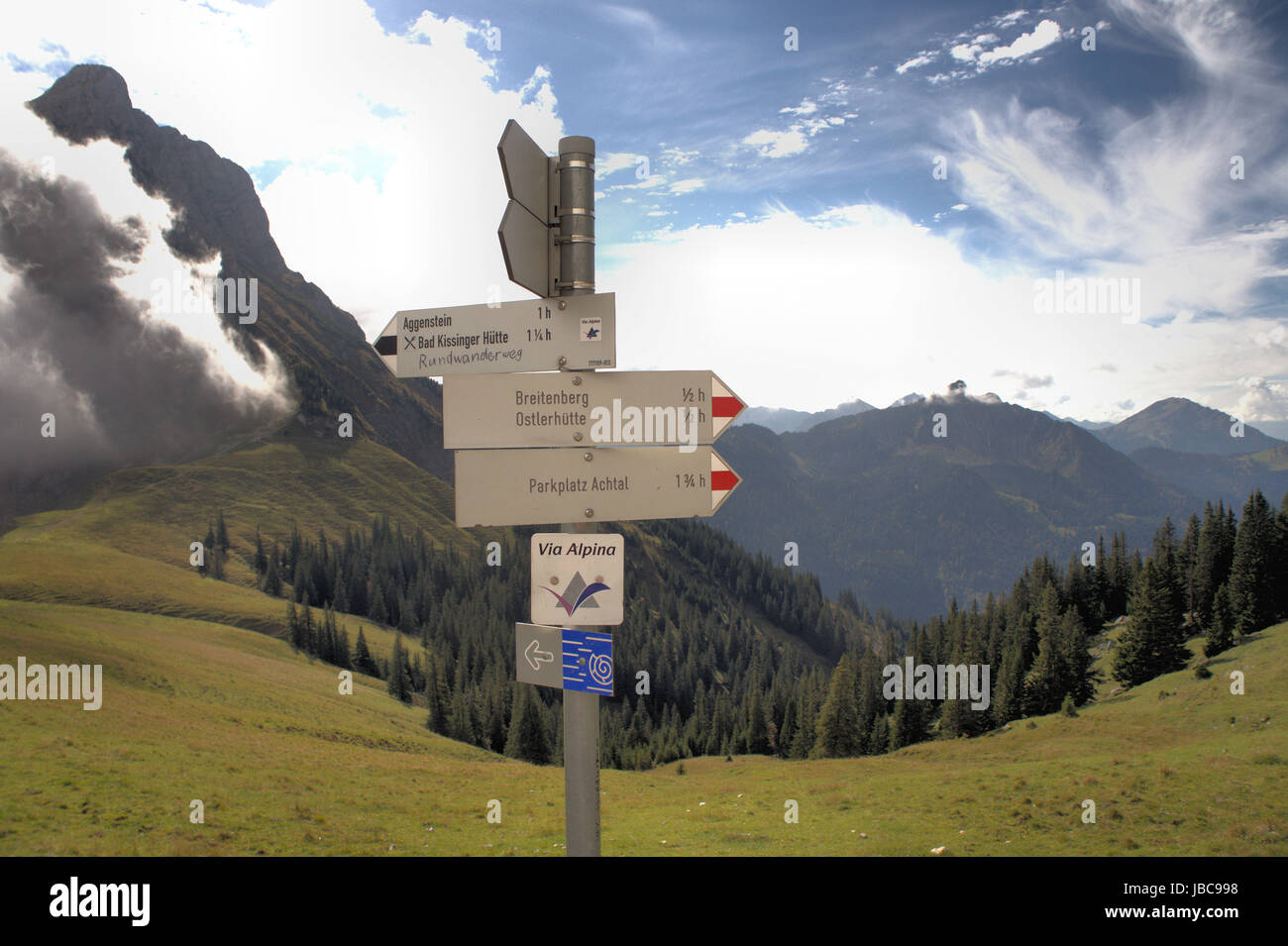 Im Vordergrund ein Wegweiser; der Aggenstein in Bayern, Deutschland und das Tannheimer Tal in Tirolo, Oesterreich; steile Felsen, weiße und dunkle Wolken; Berge und Täler, Wälder und Bergwiesen; in primo piano un cartello; il Aggenstein in Baviera, Germania e la Valle di Tannheimer in Tirolo, Austria; ripide rocce, bianco e nuvole scure, montagne e valli, boschi e prati di montagna; Foto Stock
