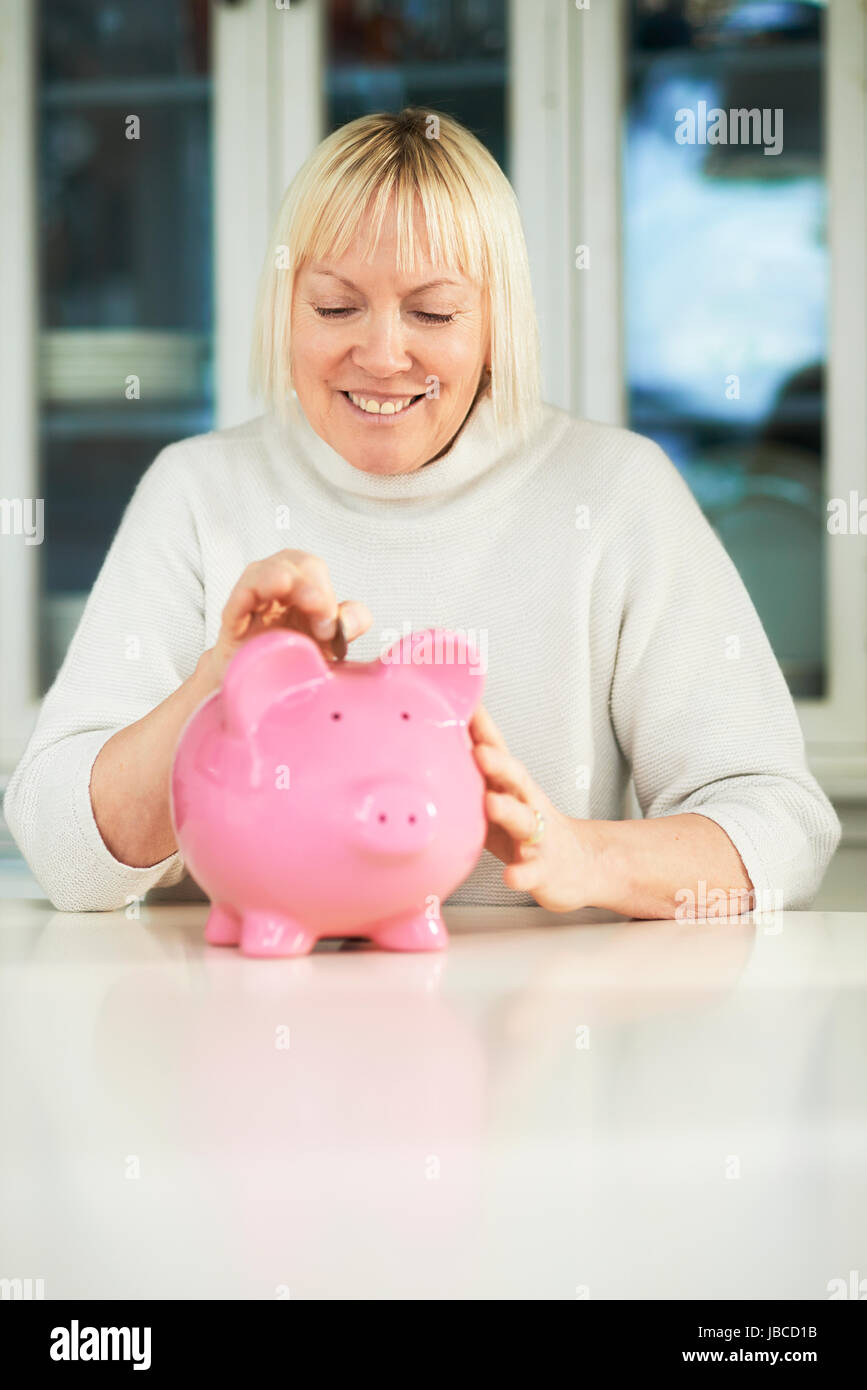 Ritratto di felice caucasica donna senior di salvataggio di monete in euro in piggybank e sorridente Foto Stock