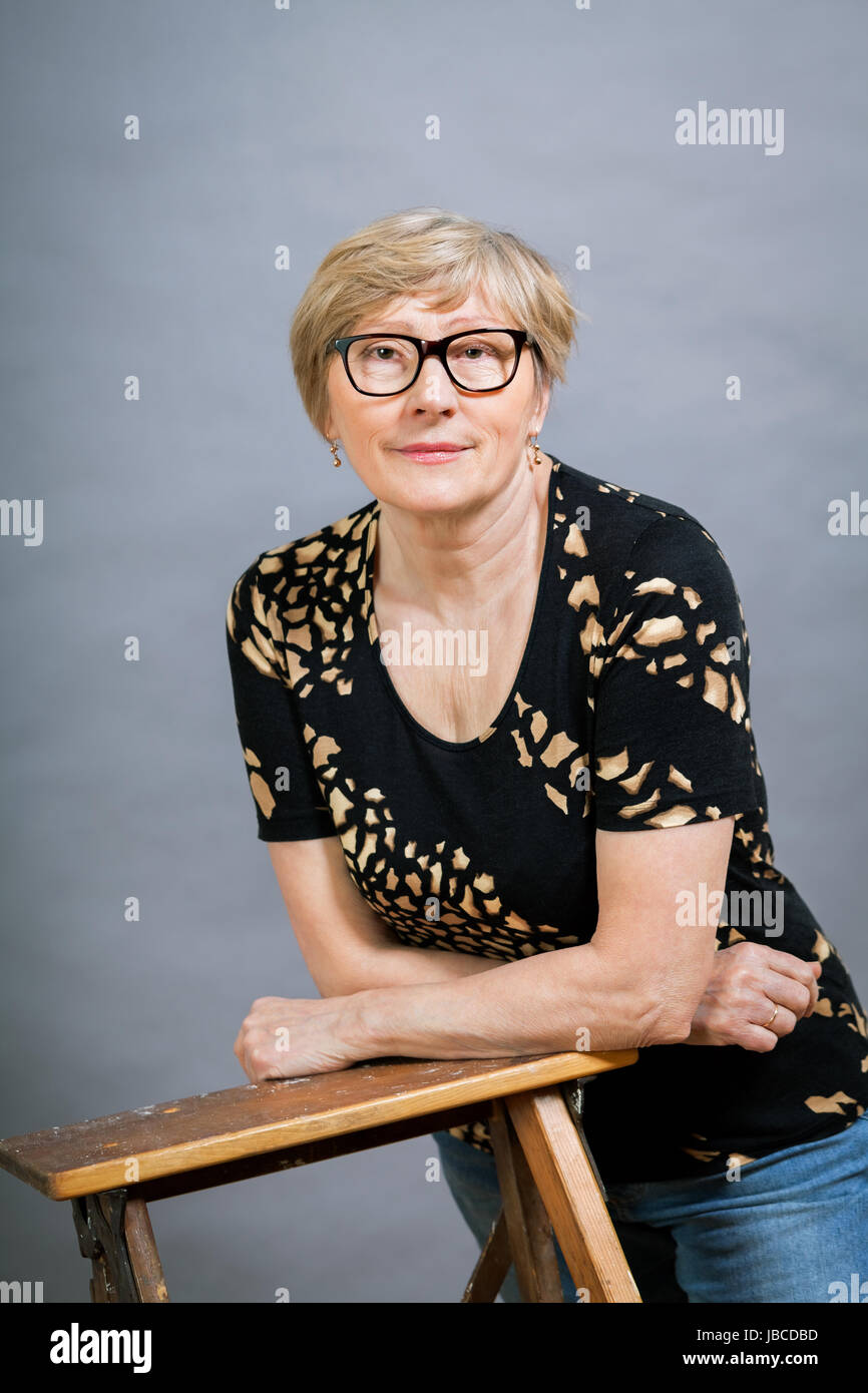 Ältere erwachsene frau seniorin mit grauen haaren und falten lachend gesund ritratto vor gauem hintergrund Foto Stock