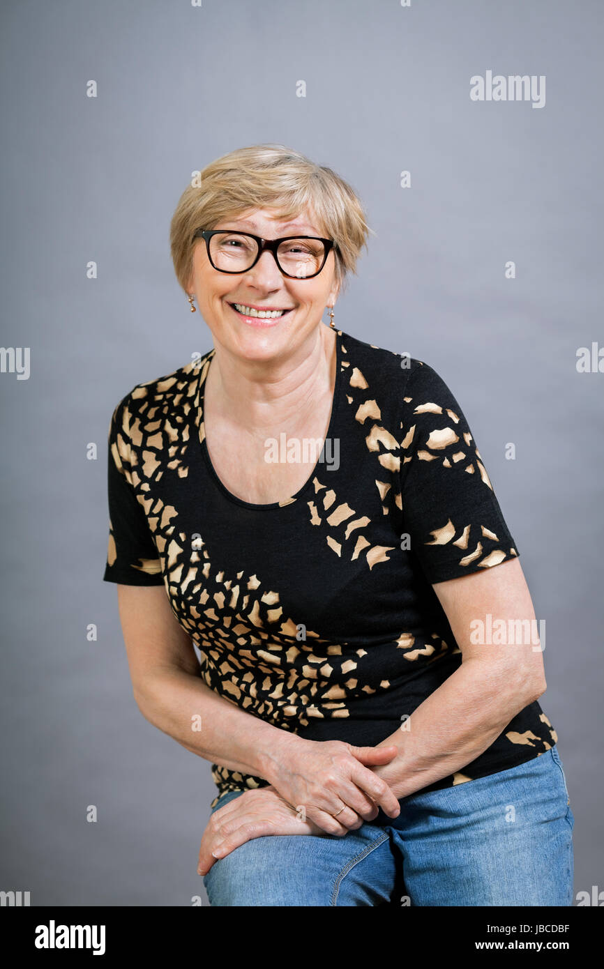 Ältere erwachsene frau seniorin mit grauen haaren und falten lachend gesund ritratto vor gauem hintergrund Foto Stock