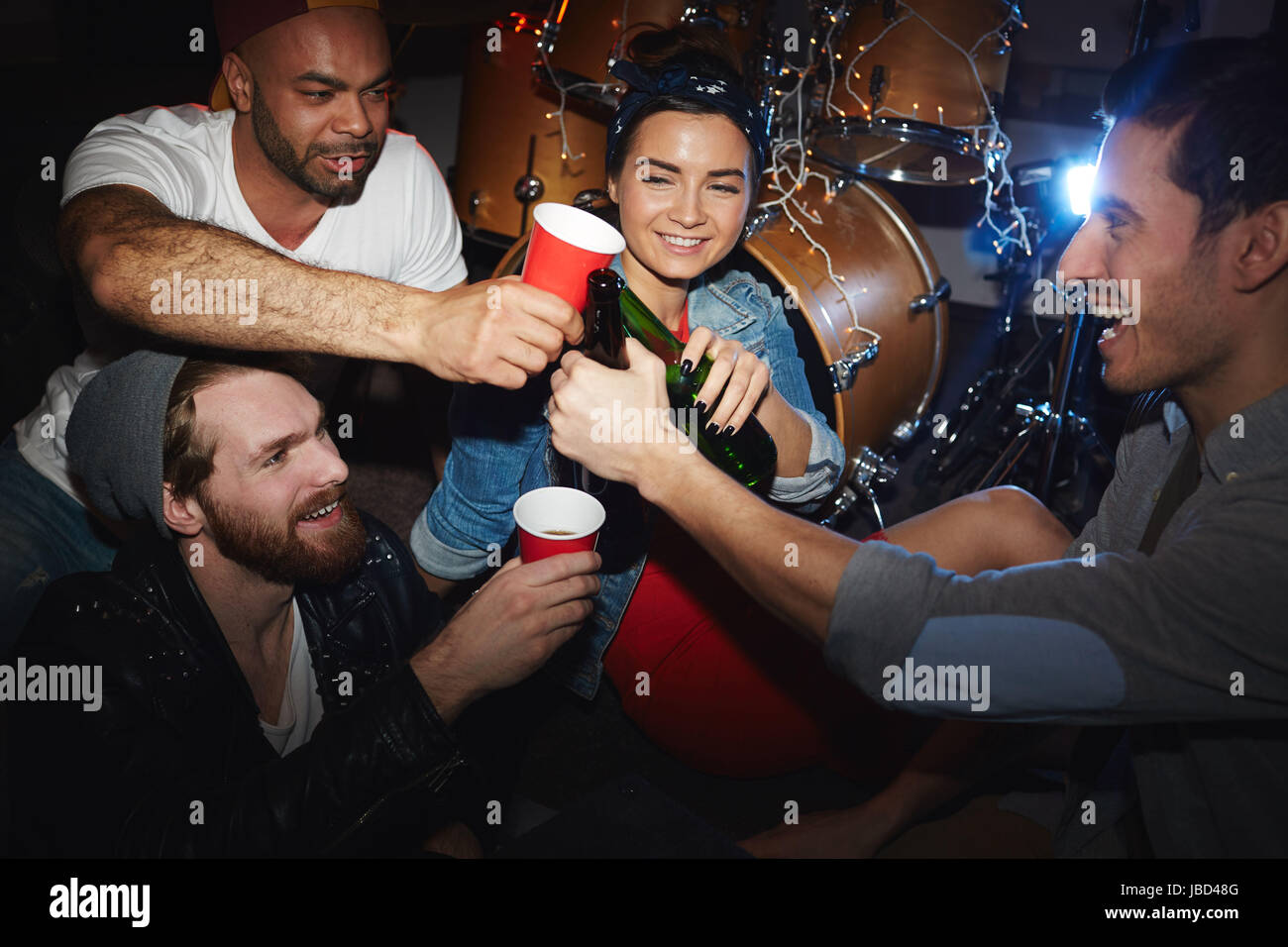 Un gruppo di giovani sorridenti party people, uomo e donna, a bere birra e sollevamento di bicchieri appendere fuori nel night club Foto Stock