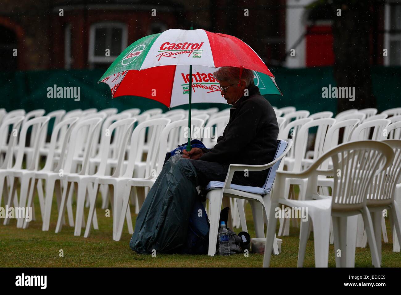 Un uomo che ripara dalla pioggia a una partita di cricket sotto un ombrello Foto Stock