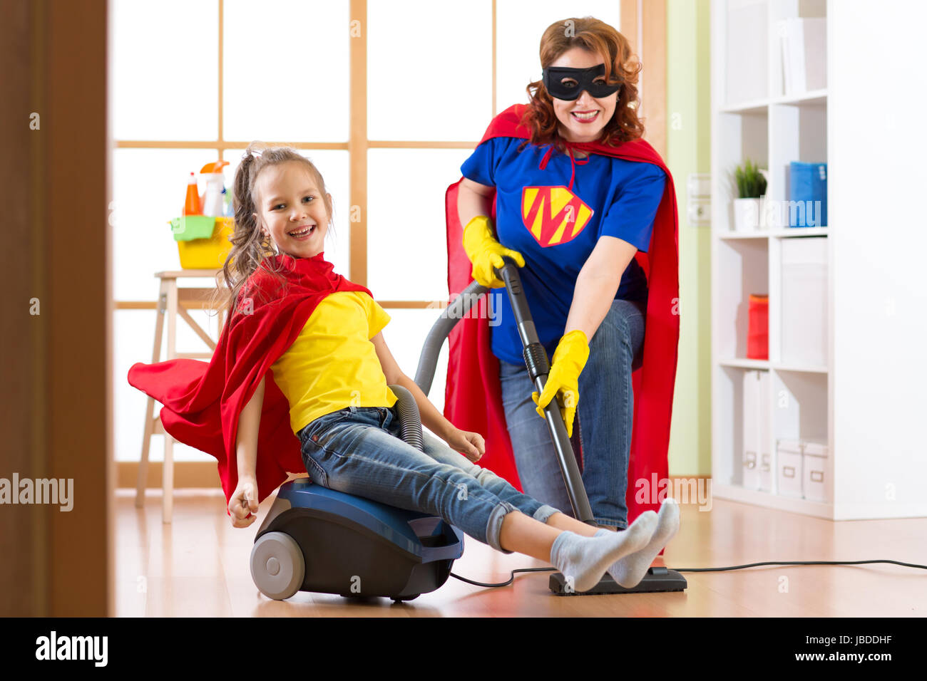 Kid ragazza e sua madre usurata costumi di supereroi. Carino bambino helper e donna rendono la pulizia camera e hanno un divertimento. Foto Stock