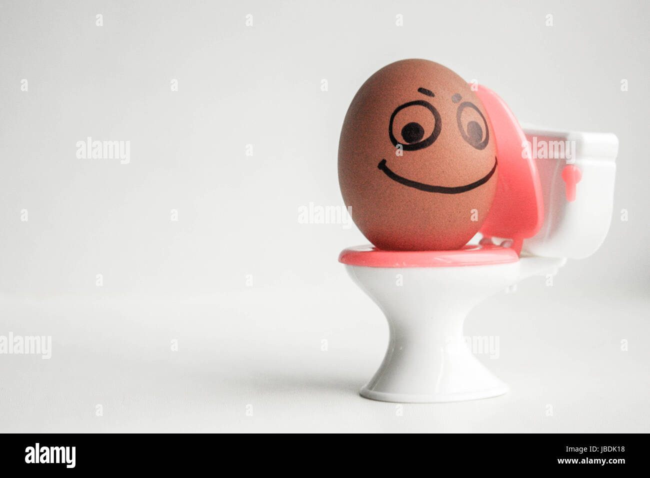 Concetto di stipsi. Un divertente di uovo con una faccia dipinta sul sedile di gabinetto si siede tuzhitsya. Foto per il tuo design Foto Stock