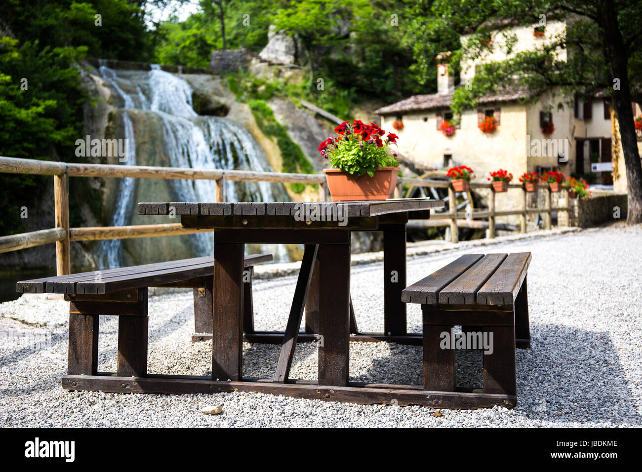 Panca con cascata e un cottage con mulino ad acqua in background Foto Stock