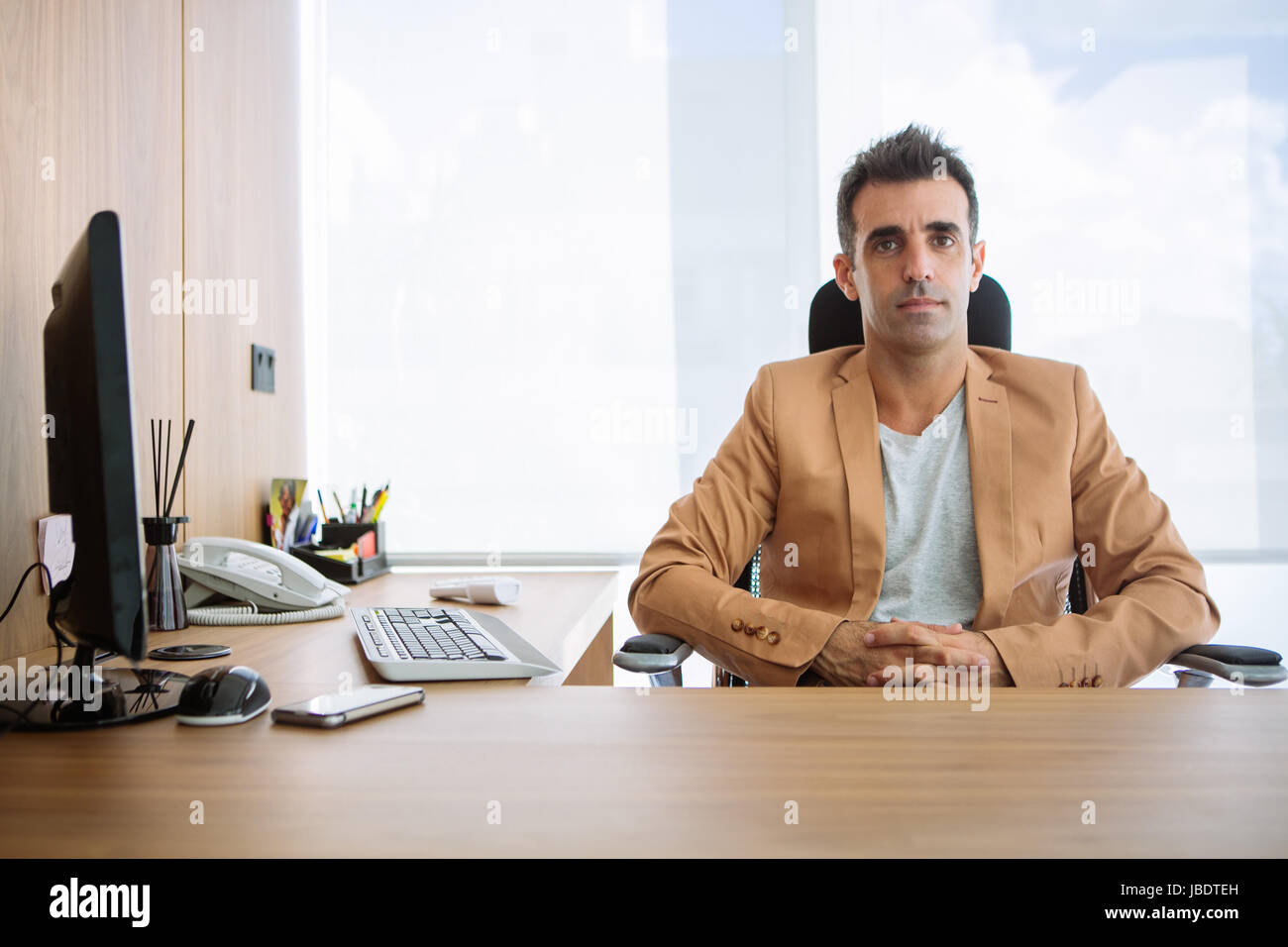 Un 35 - 40 anni uomo caucasico capelli scuri cool moderno look informale posti a sedere dietro una scrivania in una stazione di lavoro in un ufficio Foto Stock