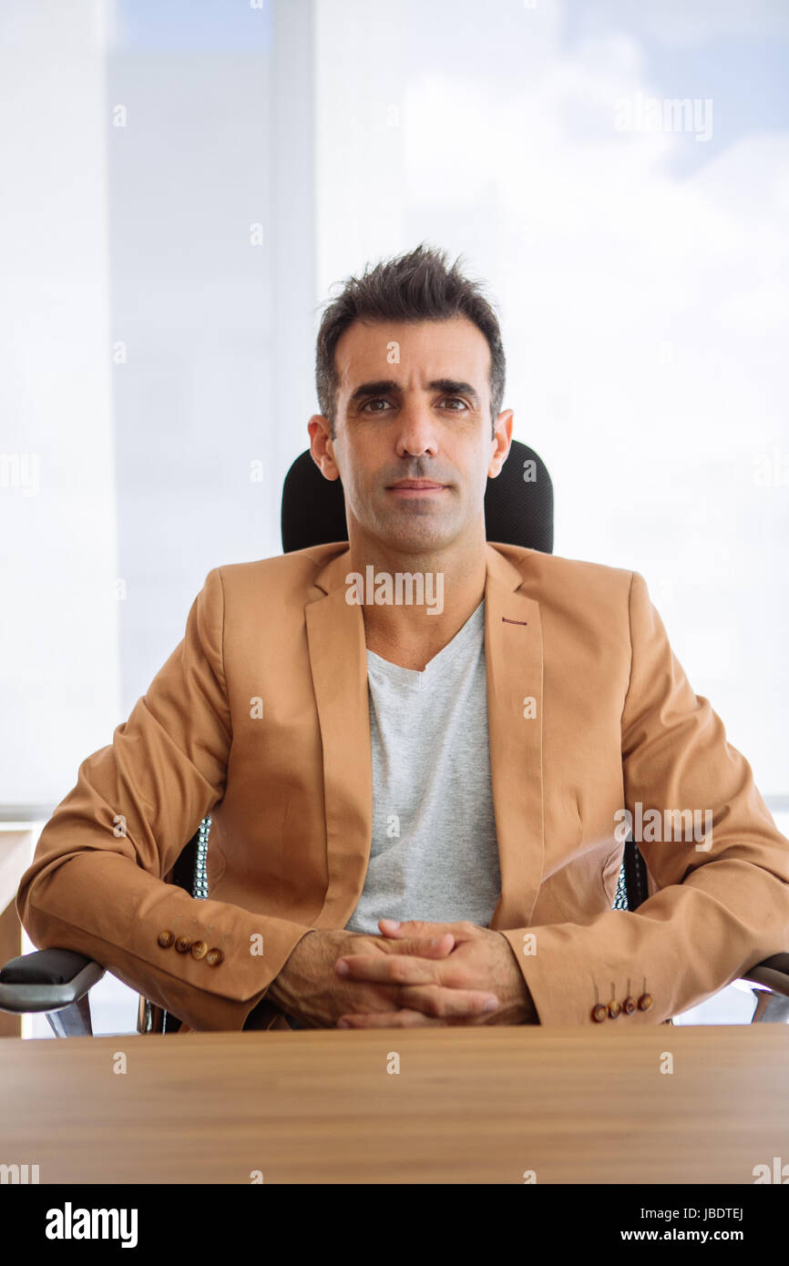 Un 35 - 40 anni uomo caucasico capelli scuri cool moderno look informale posti a sedere dietro una scrivania in una stazione di lavoro in un ufficio Foto Stock