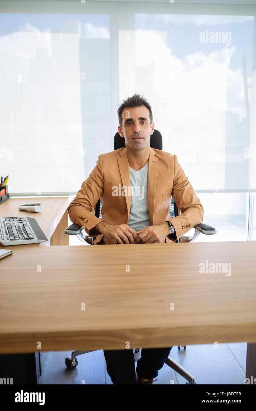 Un 35 - 40 anni uomo caucasico capelli scuri cool moderno look informale posti a sedere dietro una scrivania in una stazione di lavoro in un ufficio Foto Stock