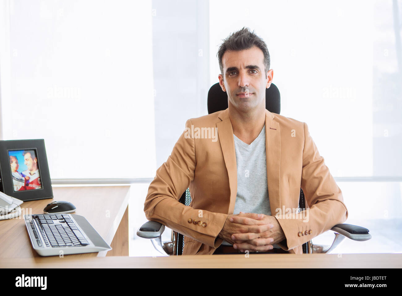 Un 35 - 40 anni uomo caucasico capelli scuri cool moderno look informale posti a sedere dietro una scrivania in una stazione di lavoro in un ufficio Foto Stock