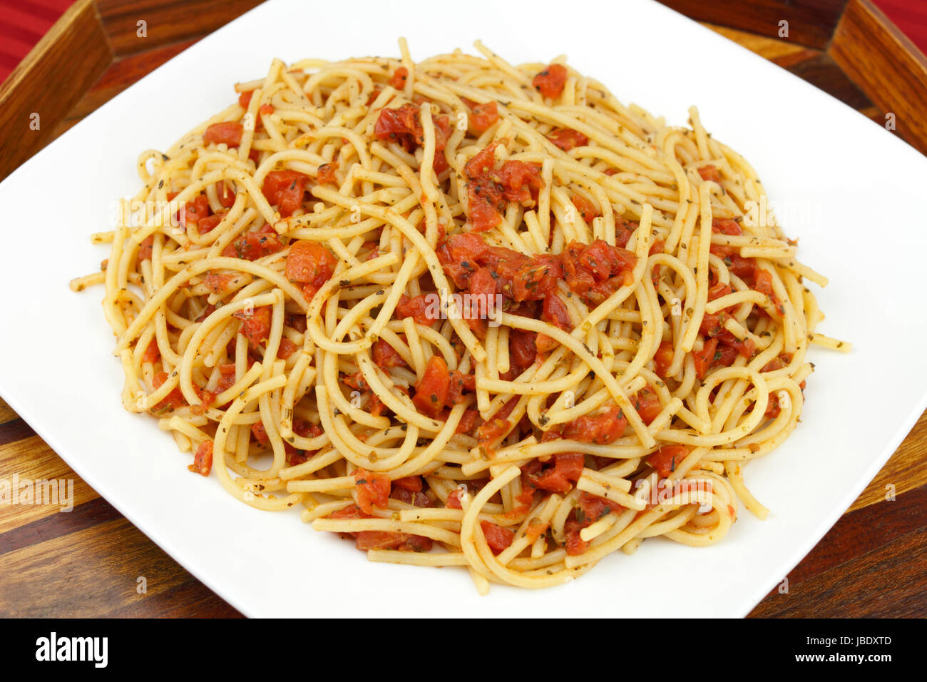 La deliziosa cena cercando di perfettamente cotti gli spaghetti noodles miscelato con organici a dadini i pomodori e le erbe serviti su una piastra bianca con belle in legno intarsiato che serve il vassoio su una tovaglia rosso. Foto Stock