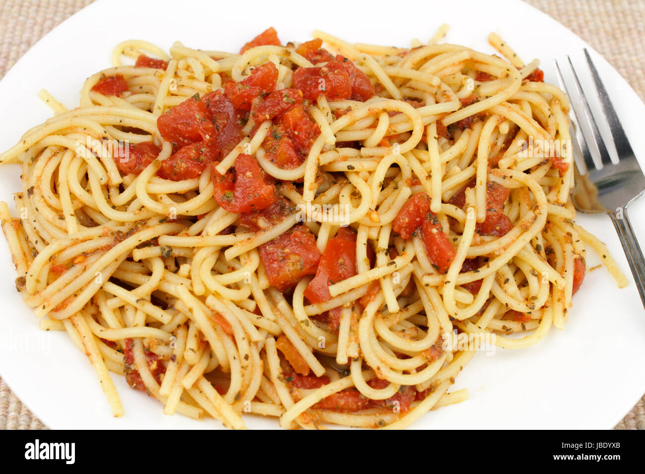 Cuocere il grano duro spaghetti miscelato con tagliare i pomodori e le erbe in un bianco rotondo piatto posto su un panno tan luogo mat. Foto Stock